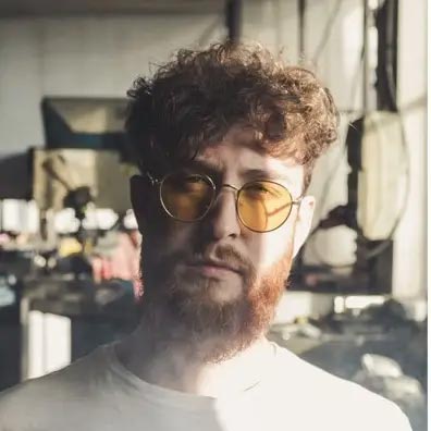Young man with dark hair and beard, brown eyes, blue t-shirt
